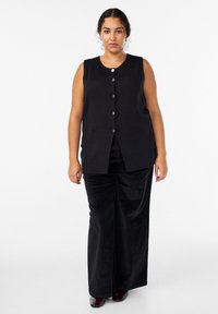 Čierny tielkový top so šiestimi striebornými gombíkmi, rovný strih, hladká textúra, kombinovaný s čiernymi širokými nohavicami z mäkkej látky.