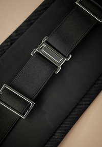 Czarny materiałowy pasek z metalowymi klamrami, charakteryzujący się teksturowaną powierzchnią i solidną konstrukcją. Przyjrzyj się z perspektywy z góry.