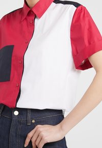 Camisa de manga corta con paneles rojos y blancos, que presenta un bolsillo azul. Fabricada en algodón suave, con detalles de botones y un corte relajado.