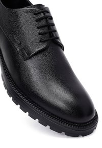 Zwarte leren schoenen met een gestructureerde afwerking, met zes veterogen, ronde neus en een dikke, geprofileerde rubberen zool.