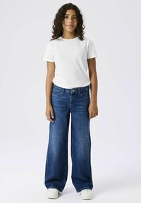 T-shirt blanc à manches courtes, associé à un jean large bleu et des baskets blanches. Tissu lisse et coupe décontractée, avec poches.
