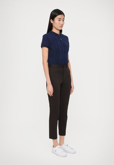 Μπλε ναυτικό πόλο πουλόβερ με κοντά μανίκια, σε συνδυασμό με μαύρο στενό παντελόνι και λευκά αθλητικά παπούτσια, παρουσιασμένα σε ουδέτερο φόντο.