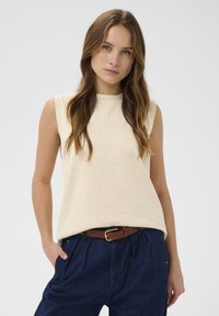 Bežinė be rankovių palaidin�ė, pagaminta iš minkštos, tekstūruotos medžiagos. Apykaklė su apvaliu iškirpimu, laisvo kirpimo, derinama su tamsiai mėlynomis raukšlėtomis kelnių ir rudą diržu.