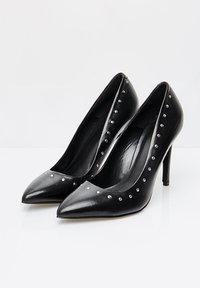Pantofi cu toc �înalt, din piele neagră, cu vârf ascuțit și dispozitive metalice argintii pe margine; textură netedă și design elegant.