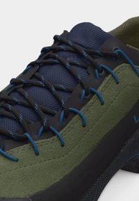 Close-up van een groene en marineblauwe sneaker met zwart-blauw patroon op de veters, geregen door blauwe oogjes.