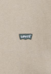 Tessuto beige con finitura testurizzata, caratterizzato da un piccolo logo ricamato di Levi's in verde e bianco a forma di ala di pipistrello.