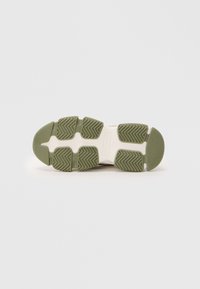 Semelle de sneaker verte et blanche avec des motifs de grip en caoutchouc texturé, présentant une forme épurée et un design de bout arrondi.