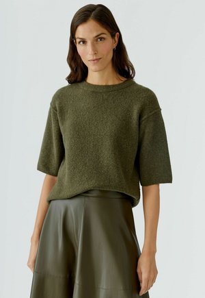 Olivgrüner gestrickter Pullover mit kurzen Ärmeln, strukturierter Stoff, runder Ausschnitt, kombiniert mit einem passenden hoch taillierten Ledrock.