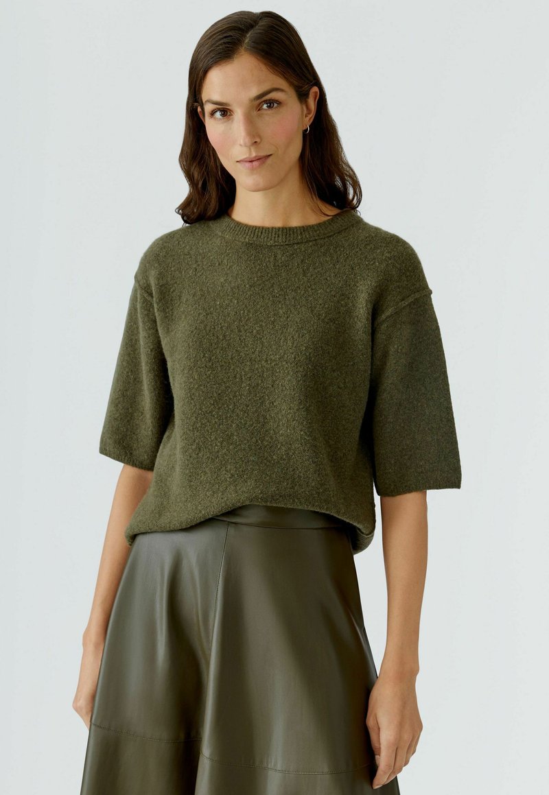Olivgrüner gestrickter Pullover mit kurzen Ärmeln, strukturierter Stoff, runder Ausschnitt, kombiniert mit einem passenden hoch taillierten Ledrock.