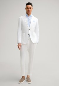 Weißer Leinenblazer und passende Hose mit einem hellblauen Hemd. Glatte Textur, zwei vordere Taschen und braune gemusterte Slipper.