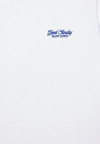 White shirt with small blue embroidered text on the chest reading "Good Sunday SLOW DOWN."