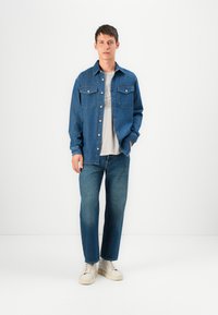 Denim košulja, tamnoplava, s dva džepa na prsima, kopčanje na dugmad i opušteni kroj, u kombinaciji s svijetloplavim trapericama i bijelim tenisicama.
