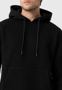 Zwarte hoodie gemaakt van een katoenmix, met een voorzak in kangoeroestijl, verstelbare koordjes en een zachte textuur.