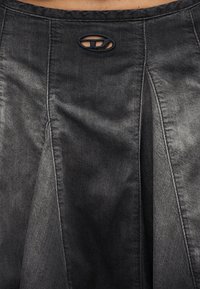 Κοντινό πλάνο μαύρης τζιν φούστας με εμφανείς ραφές και μικρή οβάλ λεπτομέρεια-κοπή κοντά στη μέση.