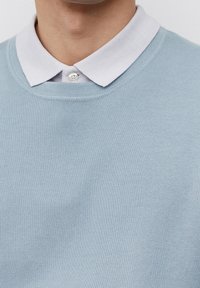 Maglione lavorato a maglia di colore azzurro chiaro con scollatura rotonda, indossato sopra una camicia bianca con colletto. Il colletto ha una chiusura a bottone e un tessuto textured.