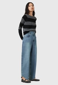 Maglione a righe nere e grigie, jeans larghi di un blu chiaro a gamba larga con orlo sfilacciato e ballerine nere con borchie argentate.