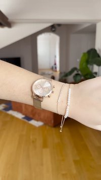 Roségoldene Armbanduhr mit rundem Ziffernblatt, drei Subdials und Netzarmband. Begleitet von zwei filigranen Armbändern, eines mit Perlen.