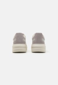 Graue Wildledersneaker mit weißen Akzenten, die über eine glatte Oberfläche, einen gepolsterten Kragen und eine dicke Plattformsohle verfügen. Leichte Verzierung an den Seiten.