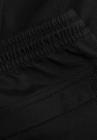 Zwarte sportbroek van een gestructureerde stof, met elastische tailleband en vlakke naden, een gladde afwerking en zonder zichtbare patronen of accenten.