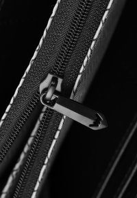 Black fabric zipper with a black pull, featuring a smooth texture and contrasting white stitching along the edge of the opening.