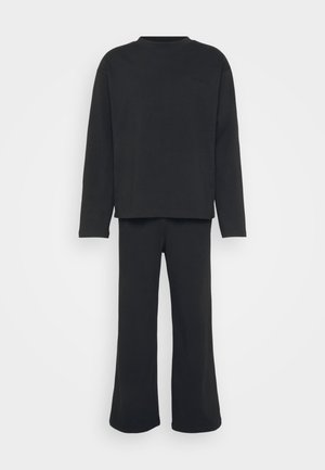 Black loungewear set including a long-sleeved top and flared pants, made of soft fabric; features a crew neckline and subtle logo detail.
