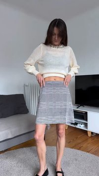 Pull blanc en maille avec un col décoratif, associé à une mini-jupe pied-de-poule noire et blanche. Texture douce, coupe décontractée, et chaussures plates noires.
