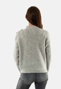 Maglione grigio chiaro con un motivo a diamante testurizzato, caratterizzato da un colletto alto e dettagli con bottoni sulla spalla, orlo a costine.