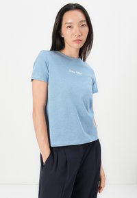 Šviesiai mėlynas medvilninis marškinėlis trumpomis rankovėmis ir apvaliu iškirpimu. Ant krūtinės puikuojasi balta "Tommy Hilfiger" siuvinėta detalė.