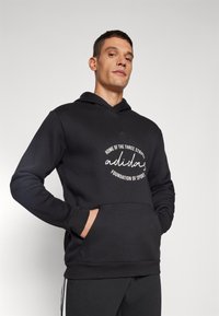 Felpa nera con cappuccio e tasca frontale, con testo bianco e logo adidas. Realizzata in materiale morbido, ha una vestibilità comoda e cappuccio.