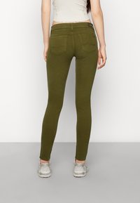 Olivově zelené fitted džíny s hladkou texturou, dvěma zadními kapsami a středně vysokým pasem. Nosit s světle zbarvenými teniskami.
