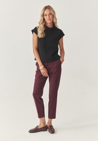 Sort kortærmet top, bordeaux skræddersyede bukser og brune loafers. Enkel design med en afslappet pasform og glat tekstur. Guldbelagt armbånd som accent.
