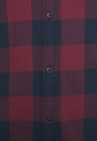 Camicia a quadri rossa e blu navy con chiusura a bottoni, caratterizzata da un tessuto testurizzato e un classico motivo a scacchi. Bottoni scuri aggiungono contrasto.