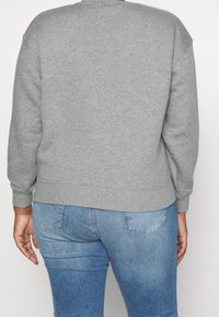 Sudadera gris con cuello redondo, puños y dobladillo acanalados. Tela de algodón suave, corte casual, vista desde la parte de atrás con jeans azules.