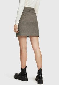 Grå randig minikjol med en åtsittande midja, bakblixtlås och subtil textur; kombinerad med kraftiga svarta ankelstövlar.