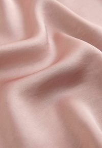 Tissu doux et lisse d'un rose pâle avec des plis délicats et des ombres subtiles, mettant en valeur la texture et les reflets de lumière.
