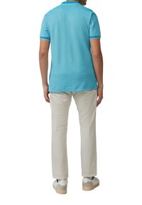 Polo turquoise à manches courtes, doté d'un col côtelé. Associé à un pantalon beige clair et des baskets blanches. Design simple et épuré.