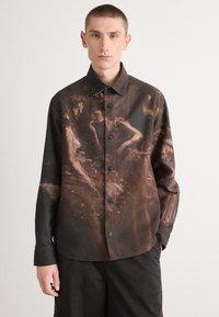 Chemise à boutonnage comportant un tissu texturé foncé avec un design pictural. Les couleurs incluent des tons marron et des nuances atténuées, avec six boutons sur le devant.