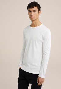 Camiseta blanca de manga larga, con un diseño ajustado y cuello redondo. La tela parece suave y lisa, combinada con jeans oscuros.