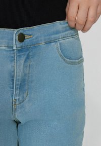 Světle modré džíny z denimu s vysokým pasem, vybavené předním zapínáním na knoflík, poutky na opasek a klasickým designem s pěti kapsami. Měkká textura.