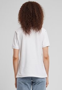 Bijela pamučna majica kratkih rukava, okruglog izreza i opuštenog kroja. Glatke teksture i uredno obrubljena, nošena s laganim plavim hlačama s uzorkom.