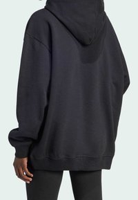 Svart oversized hoodie med dragsko i huvan, sänkta axlar och ribbade ärmslut. Tyget ser slätt ut med en matt textur.