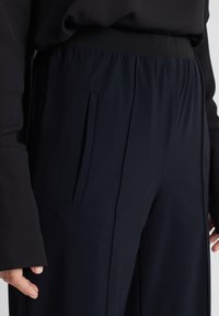 Zwarte, hoge taille broek met een brede pijp. Gemaakt van een zachte stof, met een platte tailleband en details van zijzakken.