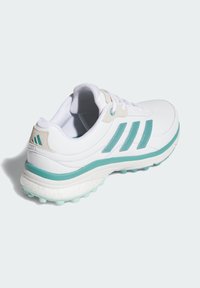 Weißer Sportschuh mit tealfarbenen Akzenten, ausgestattet mit einem Mesh-Obermaterial, gepolstertem Kragen und einer strukturierten Laufsohle mit kleinen Gummispikes für besseren Halt.