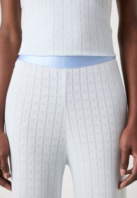 Hellblaues gestricktes Oberteil und Hose mit Herzmuster, vertikalen Streifen und einem glatten Bund. Der Stoff wirkt strukturiert und weich.