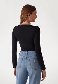 Musta pitkähihaine paita, joka on yhdistetty korkeavyötäröisiin vaaleansinisiin farkkuihin. Farkuissa on kolmikulmainen logopatchi takataskussa. Sileä rakenne.