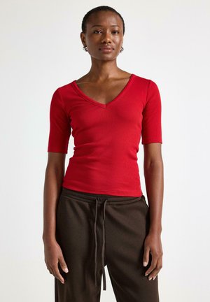 Rød ribbet V-hals kortærmet top med en tætsiddende silhuet, parret med brune sweatpants med snor. Glat tekstur, afslappet design.