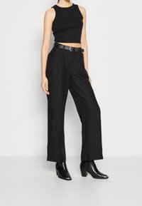 Černý zkrácený top bez rukávů, kombinovaný s širokými černými kalhotami, které jsou upevněny černým opaskem. Doplněno lesklými černými botami na podpatku, kotníkovými.