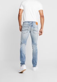 Jeans de mezclilla azul claro con un corte ajustado, que cuentan con dos bolsillos traseros y una etiqueta de cuero marrón en la cinturilla. Combinados con zapatillas blancas.