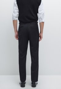 Black dress pants with a tailored fit, smooth fabric, two back pockets, and a straight leg design, paired with a gray knit vest.