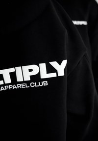 Tessuto nero con testo bianco in grassetto "ETIPLY" e testo più piccolo "APPAREL CLUB" parzialmente visibile sull'abbigliamento.